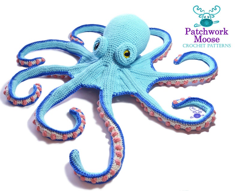 Large aqua crochet octopus with dark blue trims on its tentacles and orange bobbles on each tentacle on a white background.