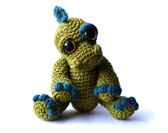 May include: A green crocheted dinosaur toy with blue accents and large brown eyes. The dinosaur is sitting with its legs outstretched.