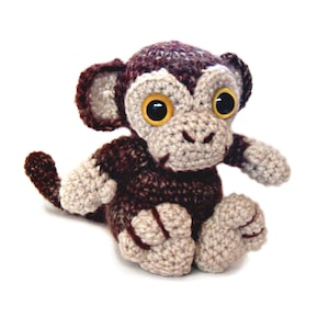 May include: A brown and beige crocheted monkey toy with large yellow eyes. The monkey is sitting with its legs crossed and its tail curled behind it.