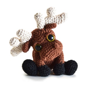 May include: A brown crocheted moose with large black eyes and white antlers. The moose is sitting with its legs tucked under its body.