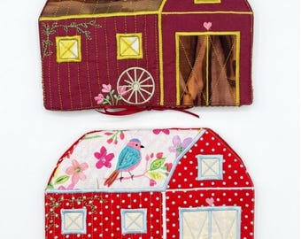 May include: Two fabric barn-shaped pot holders. The top one is deep red with a brown roof, yellow windows, and a wagon wheel. The bottom one is red with white polka dots, a floral and bird print roof, light blue windows, and a gingham tie.