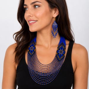 Op de afbeelding: Een kralenketting met meerdere strengen en bijpassende bungelende oorbellen in een levendig blauw en goud kleurenpalet. De sieradenset toont ingewikkelde geometrische patronen met ruitvormige motieven en lange, vloeiende kralenfranjes.