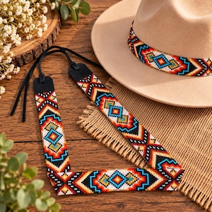 Puede incluir: Un sombrero de fieltro beige de ala ancha con una cinta a juego que presenta un patrón geométrico de cuentas rojas, naranjas, amarillas, azules y negras. Un cordón largo y fino de cuero negro está unido a la cinta, decorado con las mismas cuentas.