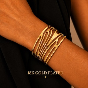Pode incluir: Uma pulseira larga composta por uma série de bandas metálicas douradas, orgânicas e onduladas, interligadas entre si. A superfície tem um acabamento polido e reflexivo. O texto 18K GOLD PLATED está impresso na parte inferior da imagem.