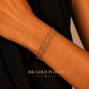 Op de afbeelding: Een set van drie 18K vergulde armbanden met verschillende kettingstijlen, waaronder een delicate kralenketting, een getextureerde schakelketting en een eenvoudige kabelketting. De tekst 18K GOLD PLATED is zichtbaar onderaan de afbeelding.