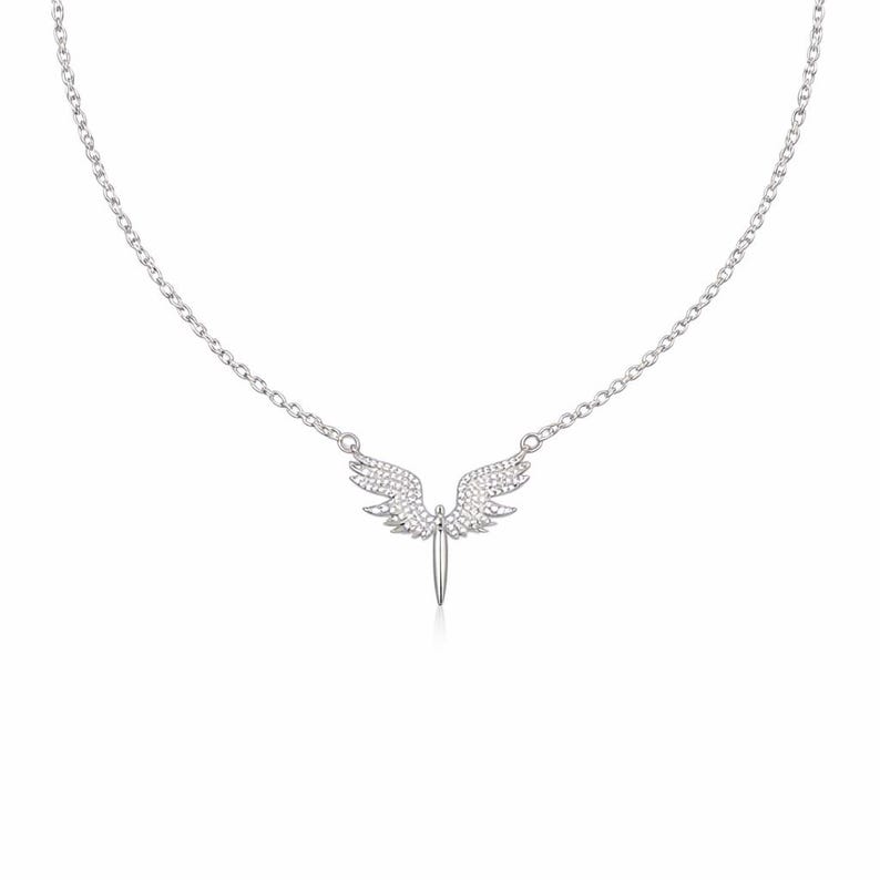 May include: A silver necklace featuring a pendant shaped like angel wings with a sword. The wings and sword are adorned with small, sparkling stones. The necklace chain is delicate and silver.