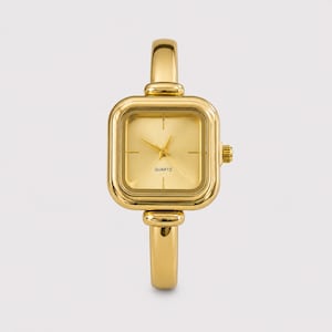 May include: A gold-toned quartz watch featuring a square face with rounded corners and a matching gold-toned metal band. The watch dial is plain gold with simple hour markers and the word QUARTZ printed in black text at the bottom center.