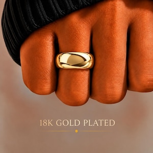 Può includere: Un anello placcato in oro 18K liscio e lucido con un design a fascia larga e arrotondata. La superficie del metallo è altamente riflettente, mostrando una brillante lucentezza dorata. Il testo 18K GOLD PLATED è visibile nell'immagine.