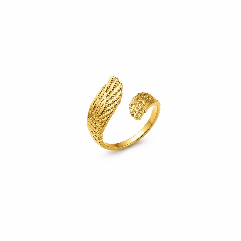 May include: A gold-colored ring with a feather design. The ring features an open design with a large feather on one side and a smaller feather on the other. The ring is made of a shiny, metallic material.