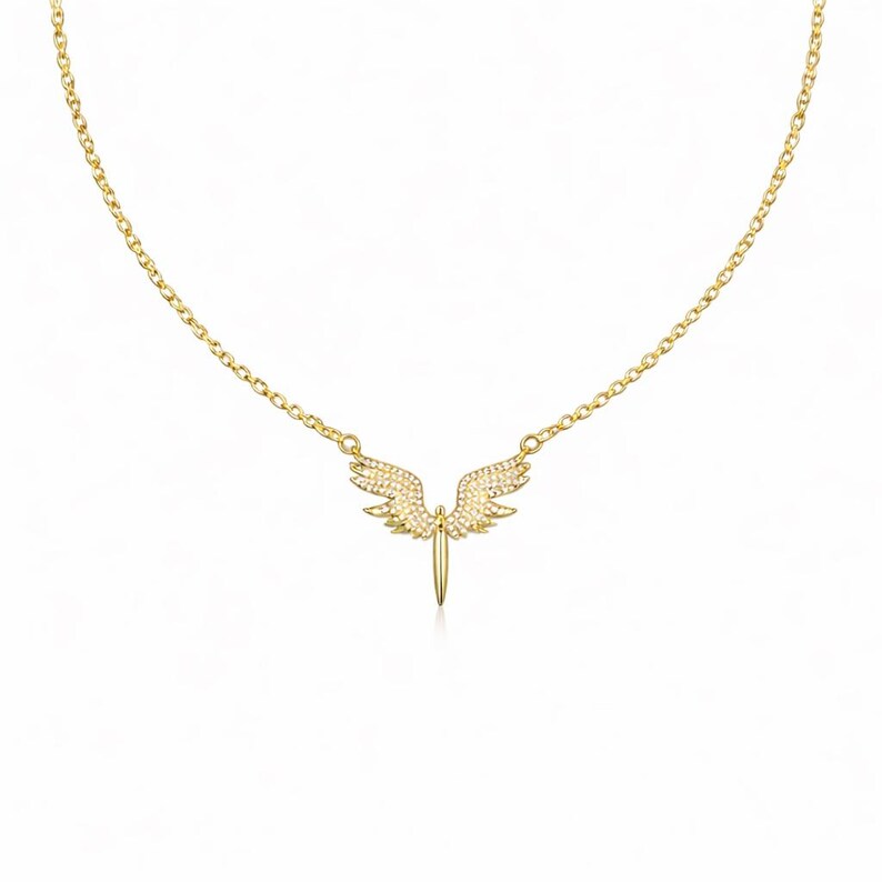 May include: A gold-colored necklace featuring a pendant shaped like angel wings. The wings are embellished with small, sparkling stones. The necklace has a delicate chain and a simple clasp.