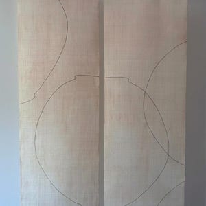 Puede incluir: Dos paneles verticales de tela beige claro colgados de una varilla de madera. La tela presenta finos dibujos de líneas de color marrón oscuro con formas circulares superpuestas y contornos de vasijas. Un pequeño sello rojo es visible abajo.