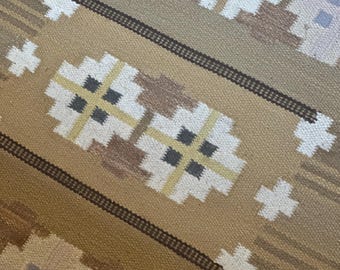 May include: A woven textile rug featuring a repeating geometric pattern in shades of tan, brown, and cream. The design includes stylized floral-like motifs with white, pale yellow, and dark gray accents, bordered by dark brown horizontal lines.