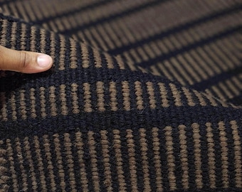 May include: A woven textile featuring a repeating pattern of thick black horizontal stripes alternating with textured brown bands. The fabric has a dense, looped pile construction with a consistent geometric design visible across the surface.
