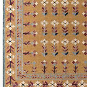 May include: Mustard-colored rug with a repeating floral pattern in white, burgundy, and blue. The border features a geometric design in similar colors, with a light blue fringe along the bottom edge. A decorative floor covering.