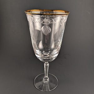 May include: A clear crystal wine glass with a gold rim and etched floral and geometric designs. The glass has a long stem and a round base, suitable for serving wine or other beverages. The glass is approximately 8 inches tall.
