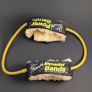May include: Joe Namath Power Bands exercise equipment. Black bands with yellow text and a yellow elastic band connecting them. The bands have a soft, beige interior and are designed for fitness.