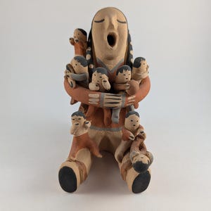 May include: A ceramic sculpture of a seated figure with an open mouth, surrounded by multiple smaller figures. The sculpture features a color palette of tan, brown, and black. The figures are arranged around the central form, creating a sense of community.