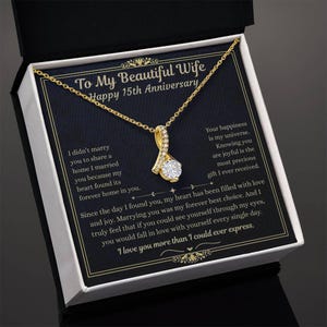 May include: A gold-colored pendant necklace with a sparkling, round, clear gemstone. The necklace is presented in a gift box with text that reads "To My Beautiful Wife Happy 15th Anniversary" and a loving message.
