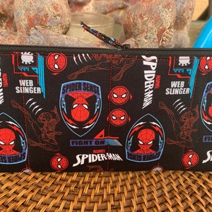 May include: Black zippered pouch with a repeating pattern of Spider-Man's face, web slinging, and the words "Spider-Sense", "Web Slinger", and "Fight On".