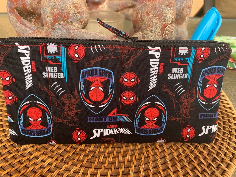 May include: Black zippered pouch with a repeating pattern of Spider-Man's face, web slinging, and the words "Spider-Sense", "Web Slinger", and "Fight On".