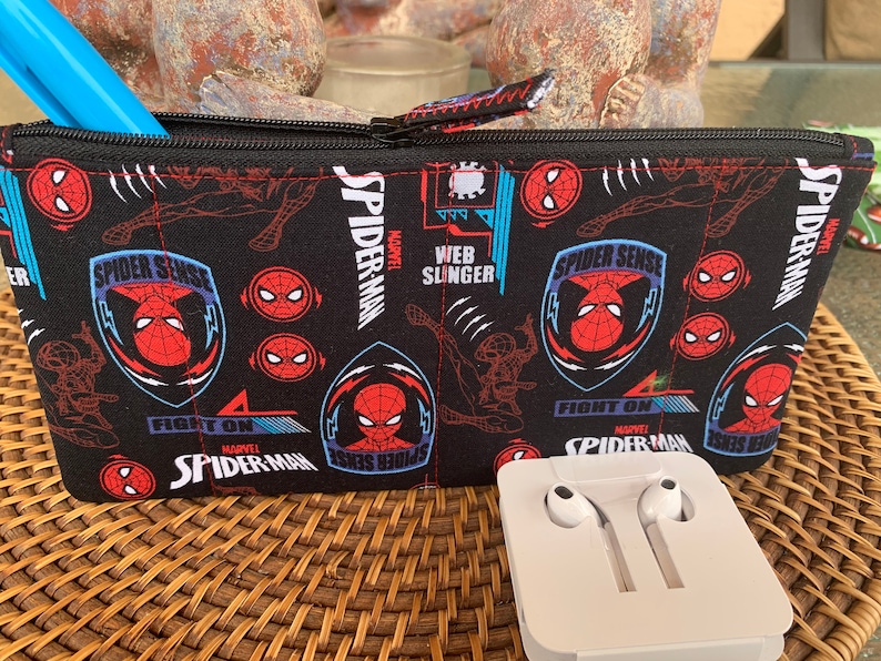 May include: Black zippered pouch with a Spiderman theme. The pouch has a repeating pattern of Spiderman's face, the words "Spider Sense", "Fight On", and "Web Slinger".