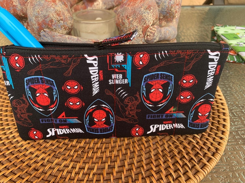 May include: Black zippered pouch with a repeating pattern of Spider-Man logos, including "Spider Sense", "Web Slinger", and "Fight On".