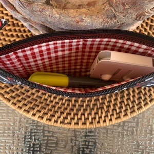 May include: A black zippered pouch with a red and white gingham lining. The pouch is open and contains a yellow highlighter and a pink phone stand.