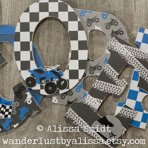 May include: Four large wooden letters spelling "CORR" in blue, gray, and white. The letters are decorated with a checkered pattern, tire tracks, and images of ATVs. The letters are arranged in a row on a wooden surface.
