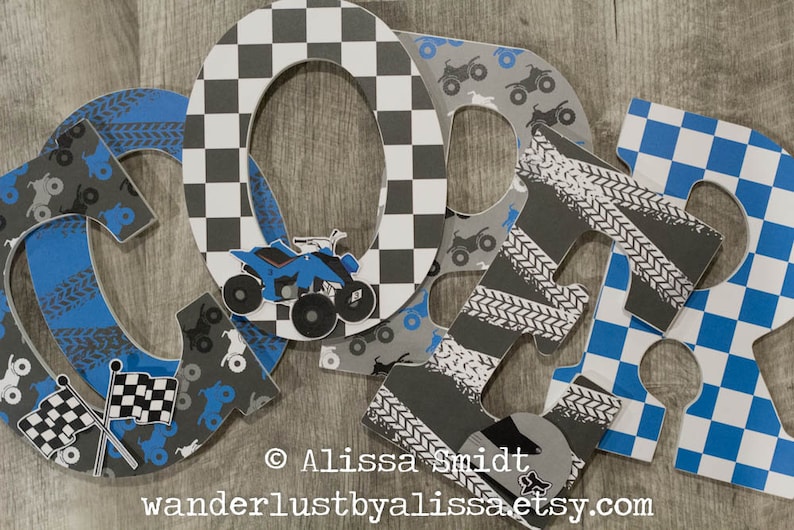 May include: Four large wooden letters spelling "CORR" in blue, gray, and white. The letters are decorated with a checkered pattern, tire tracks, and images of ATVs. The letters are arranged in a row on a wooden surface.