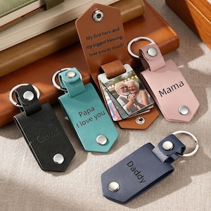 May include: Four leather keychains with metal rings and snap buttons. One black keychain says Carlos, one teal says Papa I love you, one pink says Mama, and one navy says Daddy. A brown leather keychain holds a photo of two people inside.
