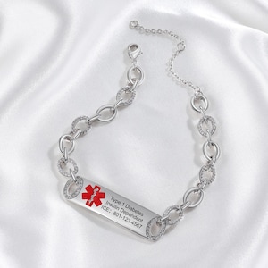 May include: A silver medical ID bracelet with a chain link design. The rectangular ID tag has a red medical symbol and text that reads "Type 1 Diabetes Insulin Dependent ICE: 801-123-4567". The bracelet is displayed on a white satin surface.