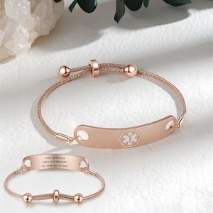 Könnte beinhalten: Roségoldenes medizinischer Notfallarmband mit geflochtenem Band und verstellbarem Verschluss. Die rechteckige Platte zeigt ein medizinisches Symbol und Text. Ein zweites Armband ist ebenfalls abgebildet mit graviertem Text: "TYPE 1 DIABETES INSULIN DEPENDENT ICE: Adiana 801-123-4567."