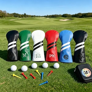 Könnte beinhalten: Eine Sammlung personalisierter Golfschlägerhauben in Schwarz, Grün, Weiß, Rot und Blau, jede mit einem individuellen Initial oder Monogramm. Golfbälle und Tees sind auf dem grünen Gras angeordnet, mit einem Golfplatz im Hintergrund.