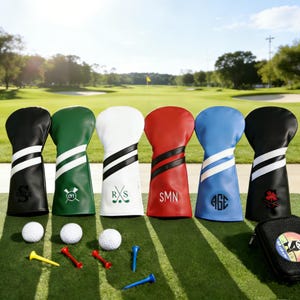 May include: A collection of personalized golf club head covers in black, green, white, red, blue, and black. Each cover has a unique design with initials or symbols. Golf balls and tees are arranged on a green surface, with a golf course in the background.