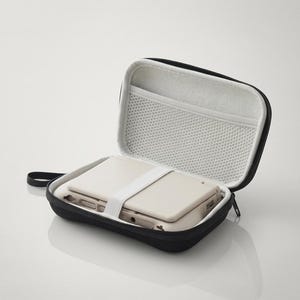 May include: A black zippered carrying case with a white interior lining and a mesh pocket. Inside the case, a beige handheld electronic gaming device is secured in place by a white elastic strap that runs across the center of the device.