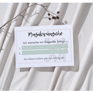 May include: A white card with the text "Musikwünsche" and lines for song requests. The card has the text "Ich wünsche mir folgende Songs..." and "Bei diesen Liedern geh ich richtig ab!". A sprig of a plant is in the upper left corner.