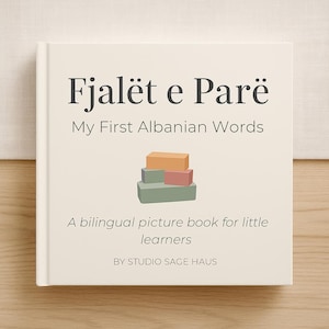 May include: A hardback book with a cream cover, titled "Fjalët e Parë" and "My First Albanian Words." The cover shows a stack of coloured blocks and the text "A bilingual picture book for little learners" and "BY STUDIO SAGE HAUS."