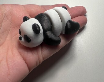May include: A 3D-printed panda figurine in black and white. The panda is lying down, with its body segmented. The head and body sections are white, while the limbs and a section of the body are black. The panda has small black ears and eyes.