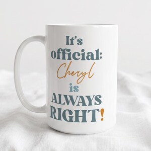 May include: White ceramic mug with the text "It's official: Cheryl is ALWAYS RIGHT!" in teal and orange lettering. The mug has a large handle and is set against a white background.