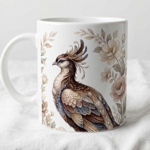 May include: White ceramic mug featuring a detailed watercolor illustration of a bird with ornate plumage and floral accents. The bird is primarily brown, beige, and blue, with a decorative crest. The mug is labeled "11 oz".