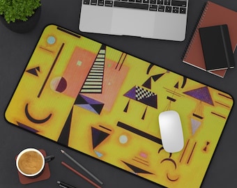 May include: A rectangular mousepad with a yellow background and a colorful abstract design featuring geometric shapes in orange, purple, black, and white. A white computer mouse sits on the pad, with a laptop and notebook in the background.