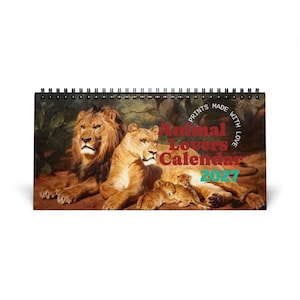 Puede incluir: Un calendario horizontal de espiral para 2027 con una pintura de una manada de leones que incluye un león, una leona y dos cachorros. El texto "Animal Lovers Calendar 2027" está impreso en rojo y turquesa, con "PRINTS MADE WITH LOVE" en un círculo.