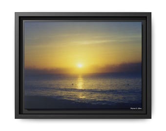 Puede incluir: Impresión en lienzo enmarcada de un amanecer sobre el océano. El cielo transita del azul al amarillo, con el reflejo del sol en el agua. La impresión está en un marco negro, con la firma del artista en la esquina inferior derecha.