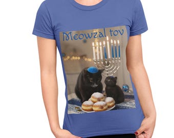 May include: Blue t-shirt featuring a graphic of two black cats wearing yarmulkes, a menorah, and sufganiyot. The text "Meowzal tov" is above the graphic. The shirt is a solid blue color.