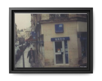 Puede incluir: Impresión enmarcada de una escena callejera frente a un edificio con la palabra "BRED" sobre la puerta. Una persona camina por la acera. La imagen tiene una estética vintage, ligeramente borrosa.