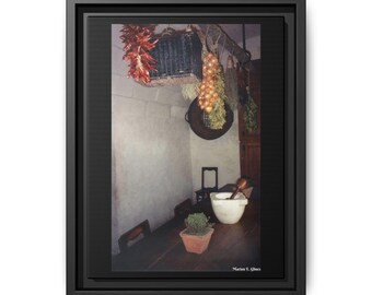 Puede incluir: Impresión en lienzo enmarcada de una escena de cocina rústica. Pimientos rojos, cebollas y hierbas cuelgan del techo. Una mesa de madera tiene una planta en maceta, un mortero y una maja, y una cuchara de madera. La imagen tiene un ambiente cálido.