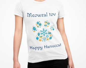 May include: White t-shirt with blue text and a paw print design. The text reads "Meowzal tov" and "Happy Hanuccat". The paw print is made up of blue and yellow Hanukkah-themed icons, including dreidels and menorahs.