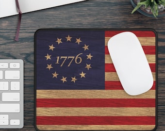 Peut inclure: Tapis de souris avec un motif de drapeau américain vieilli, avec le texte "1776" entouré d'étoiles. Le tapis a une bordure noire et est présenté avec une souris d'ordinateur blanche.