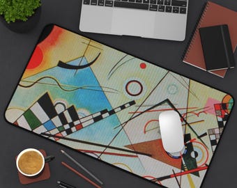 May include: A rectangular mouse pad featuring a colorful abstract design with geometric shapes, lines, and circles in red, blue, yellow, and black. A white computer mouse is on the pad, with a laptop, notebook, and coffee cup nearby.
