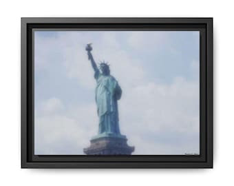 Puede incluir: Impresión en lienzo enmarcada de la Estatua de la Libertad contra un cielo azul nublado. La icónica estatua es de color turquesa, sosteniendo una antorcha en alto. La impresión está en un marco negro.